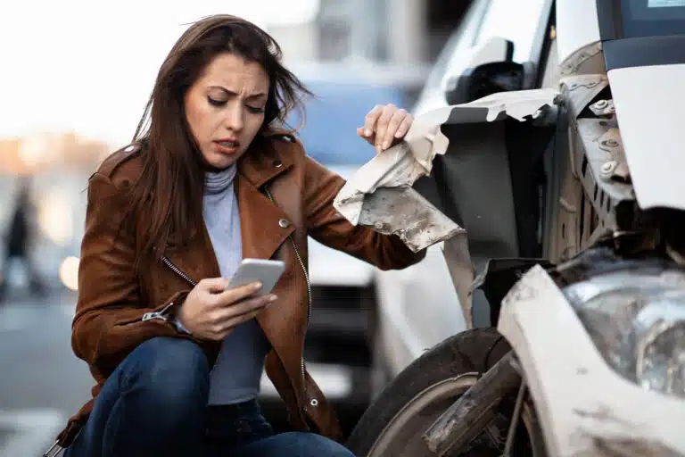 Displeased woman using cell phone and texting after a car accident in the city.