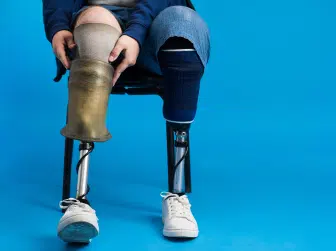 Man adjusting prosthetic leg while seated against a blue background.