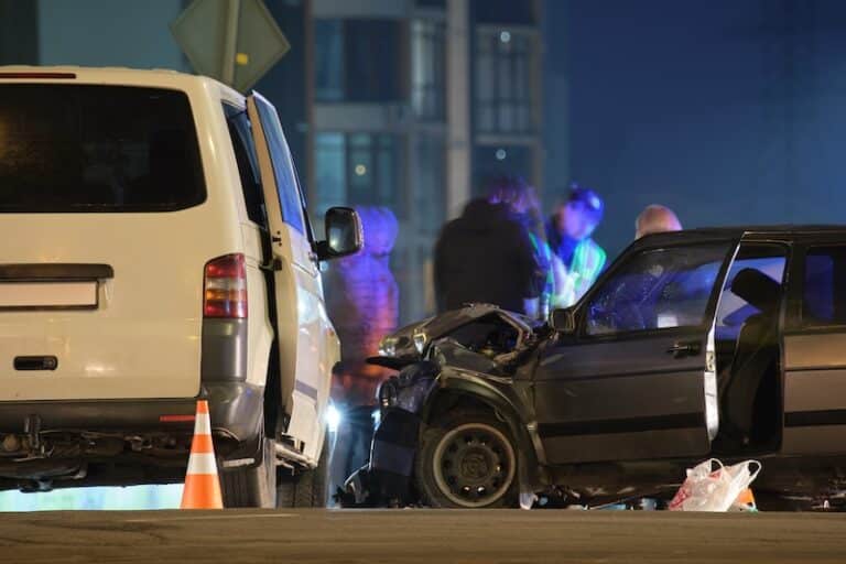 Cars crashed heavily in road accident after collision and silhouette of people on city street at night. Road safety and insurance concept