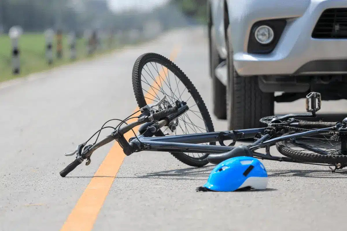 Bicycle and helmet lying on a paved road Infront of a car