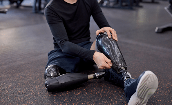 Athlete with prosthetic legs adjusting gear during a gym workout.