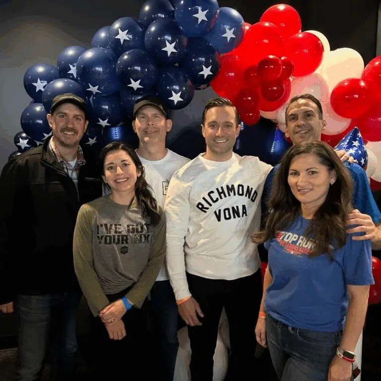 Richmond Vona team posing under a patriotic balloon arch at the Veterans Race event.