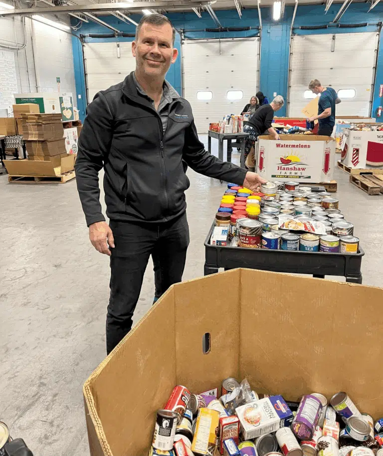 Keith Vona standing beside donated food items during a community outreach activity