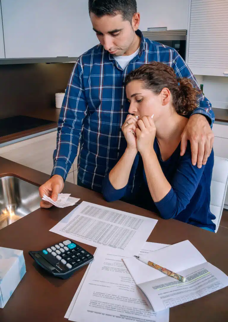 Couple iwth documents, pencil, and calculator as they are going through financial hardship/reviewing insurance policies
