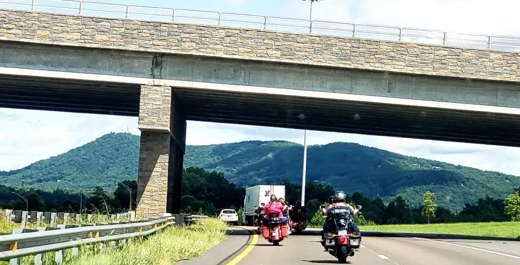 Car behind motorcycles on highway with mountains in the background