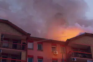 Firefighter on a balcony directed hose towards the burning building at night. Firefighters using extinguishing water. Firemen fighting a raging fire.