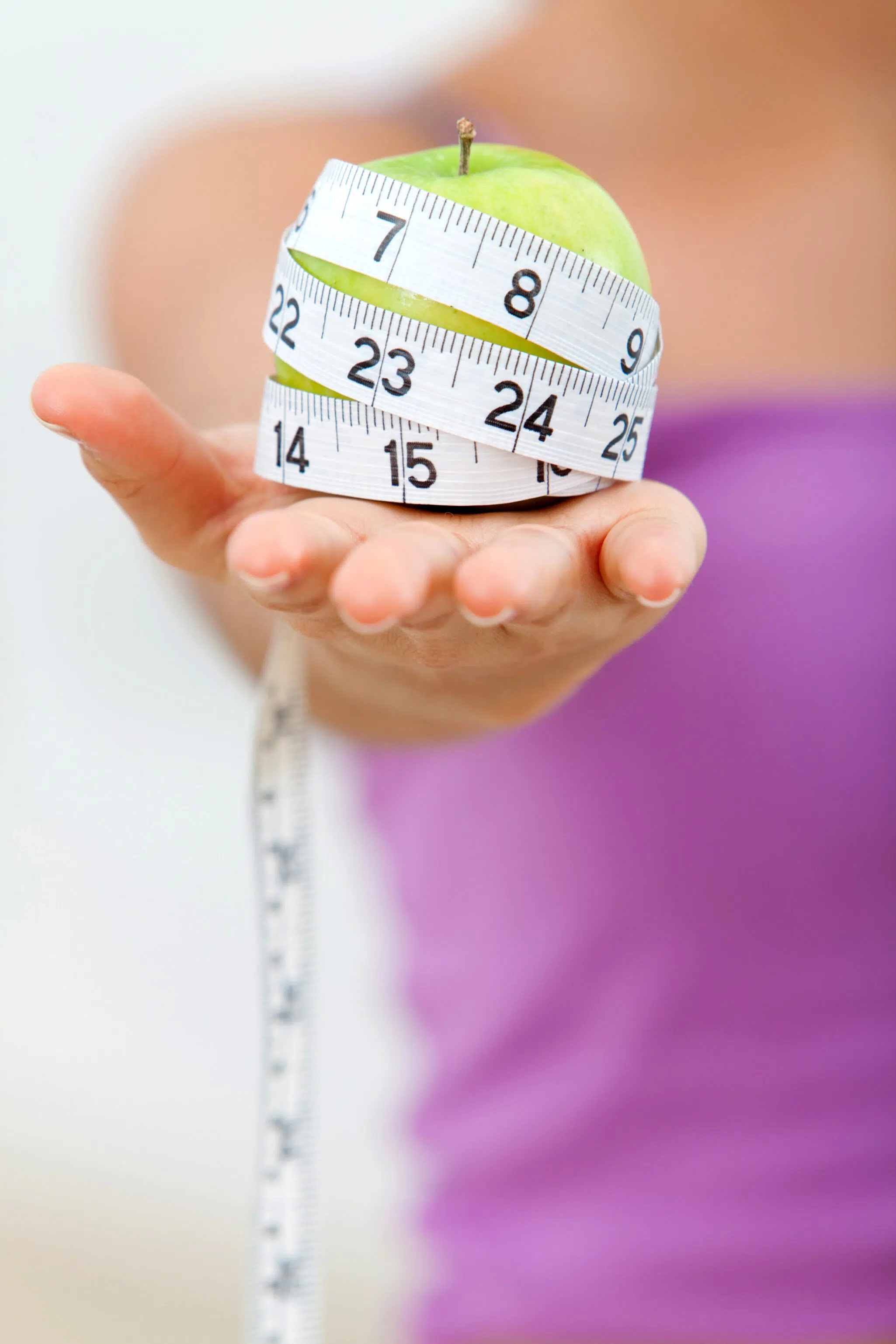 Woman holding apple with measuring tape around it