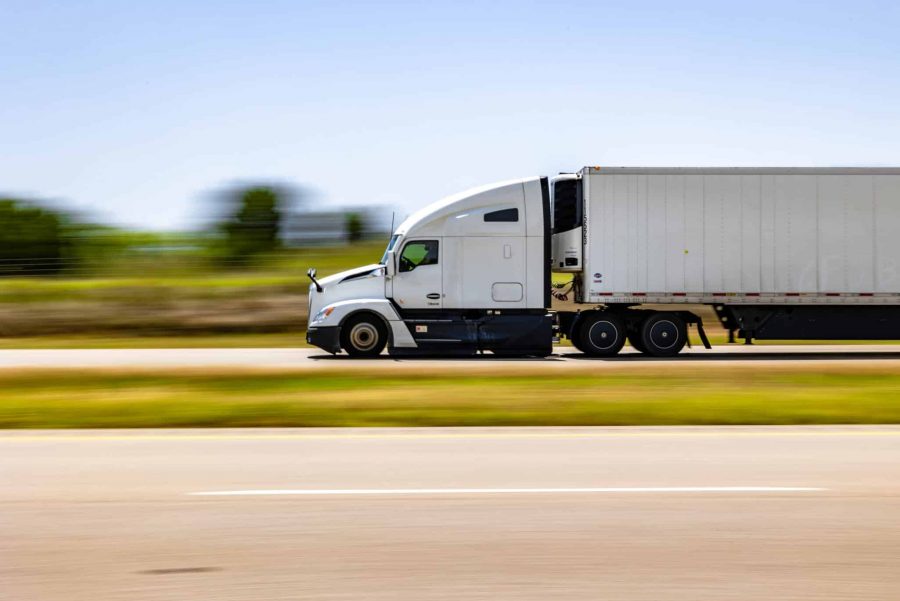 semi truck driving on a rural road with trees in the background