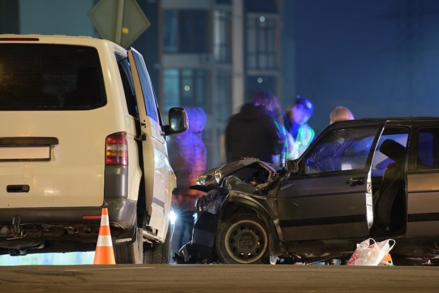 Cars crashed heavily in road accident after collision and silhouette of people on city street at night. Road safety and insurance concept