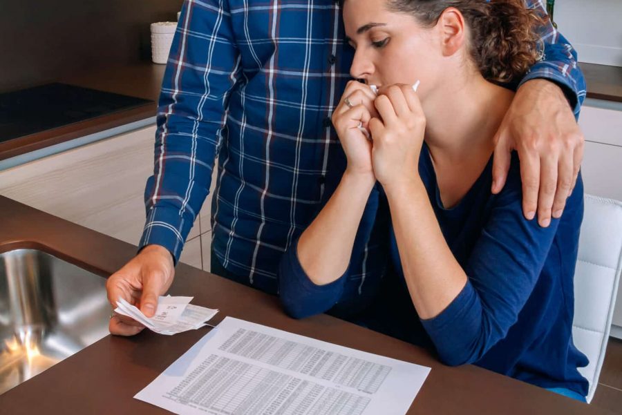 Couple iwth documents, pencil, and calculator as they are going through financial hardship/reviewing insurance policies